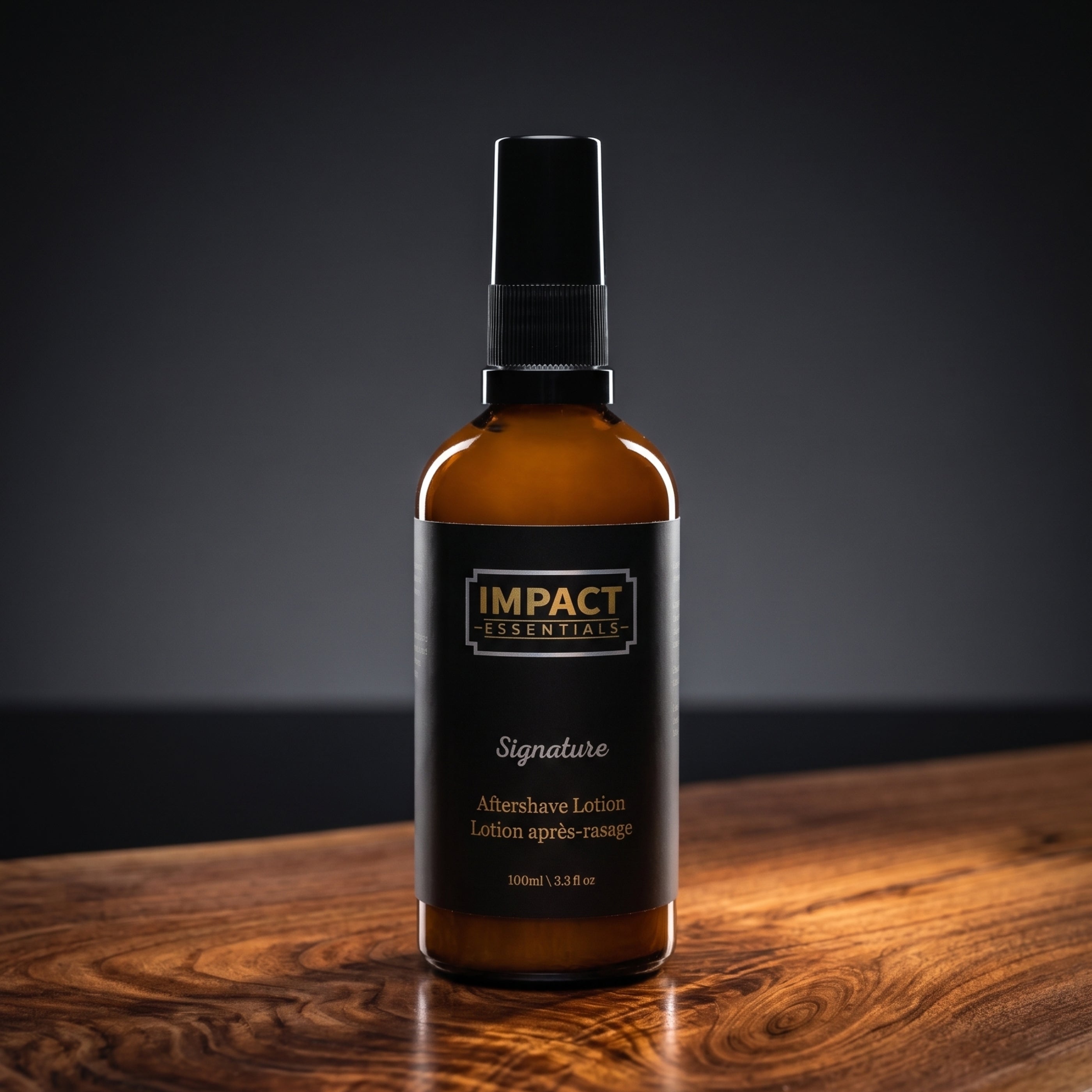 An amber glass spray bottle of Impact Essentials Signature Altershare Lotion with a black pump and black label, set on a polished wooden surface against a dark gray background.