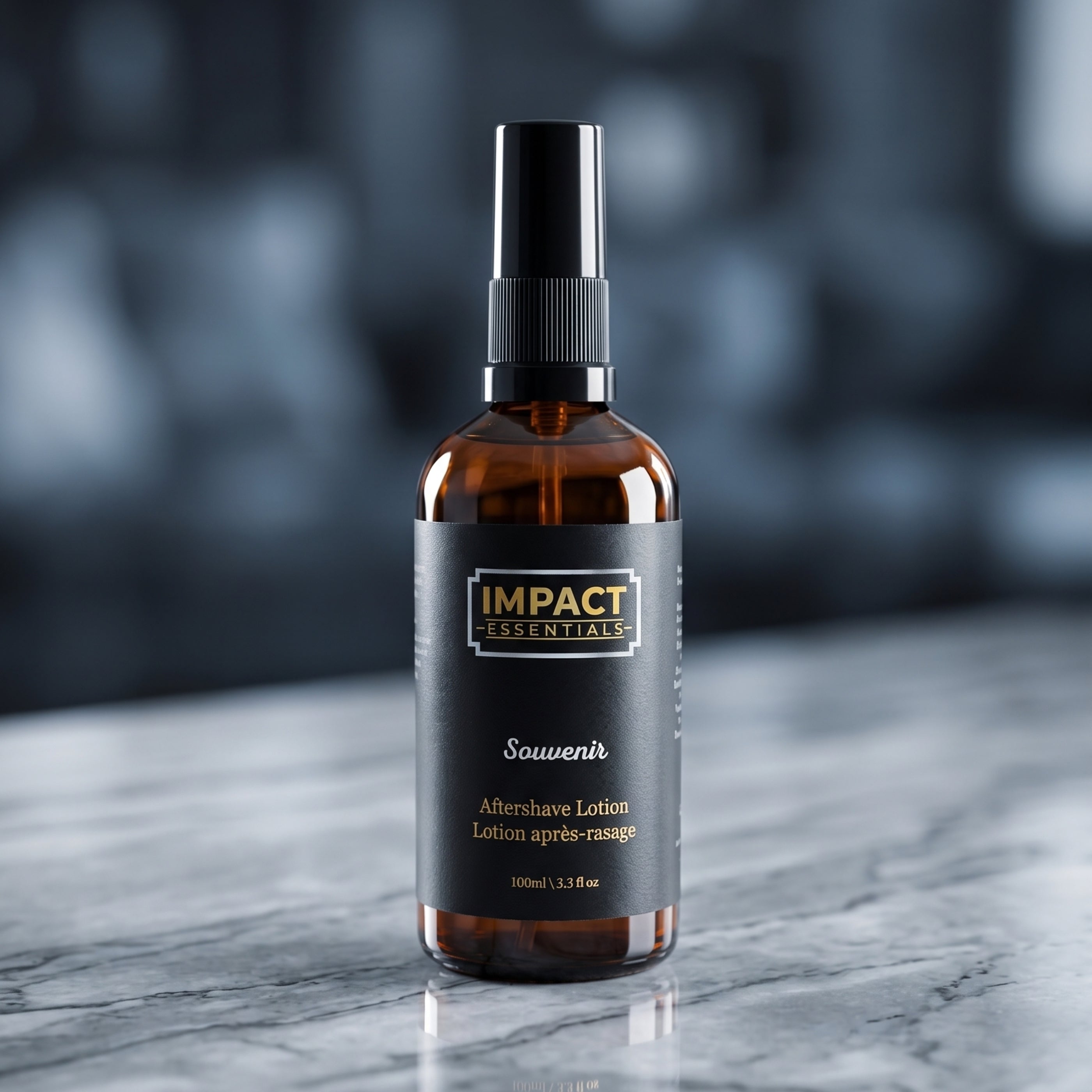 An amber glass spray bottle of Impact Essentials Souvenir Aftershave Lotion with a black spray top and black label, set on a gray marble surface with a blurred dark background.