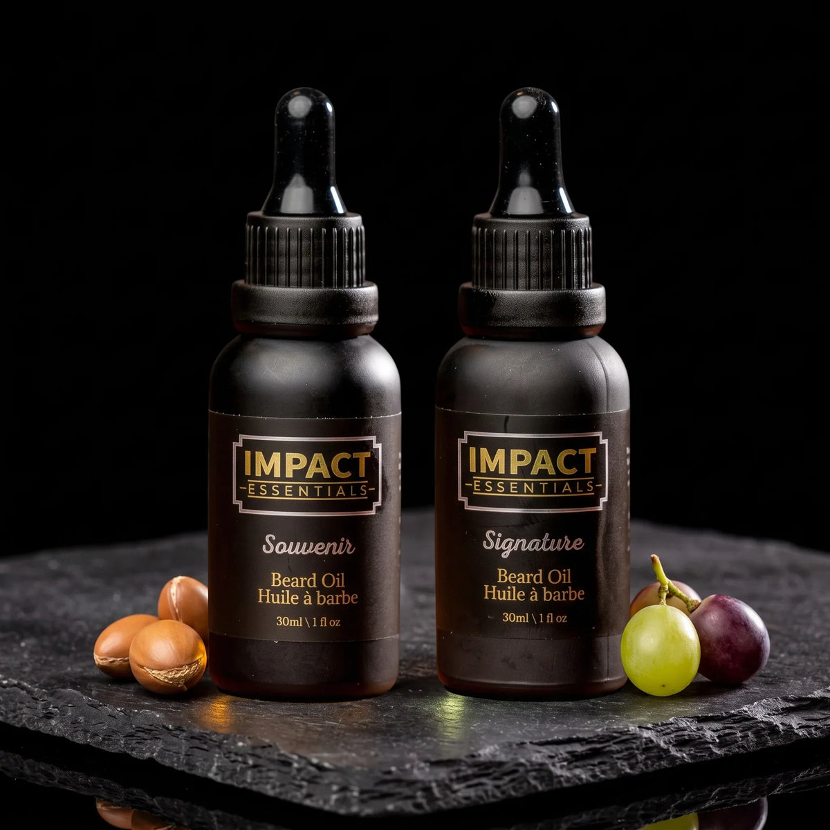 Argan vs grape seed oil - Two amber glass bottles of golden argan and clear grape seed botanical carrier oils displayed on dark slate.