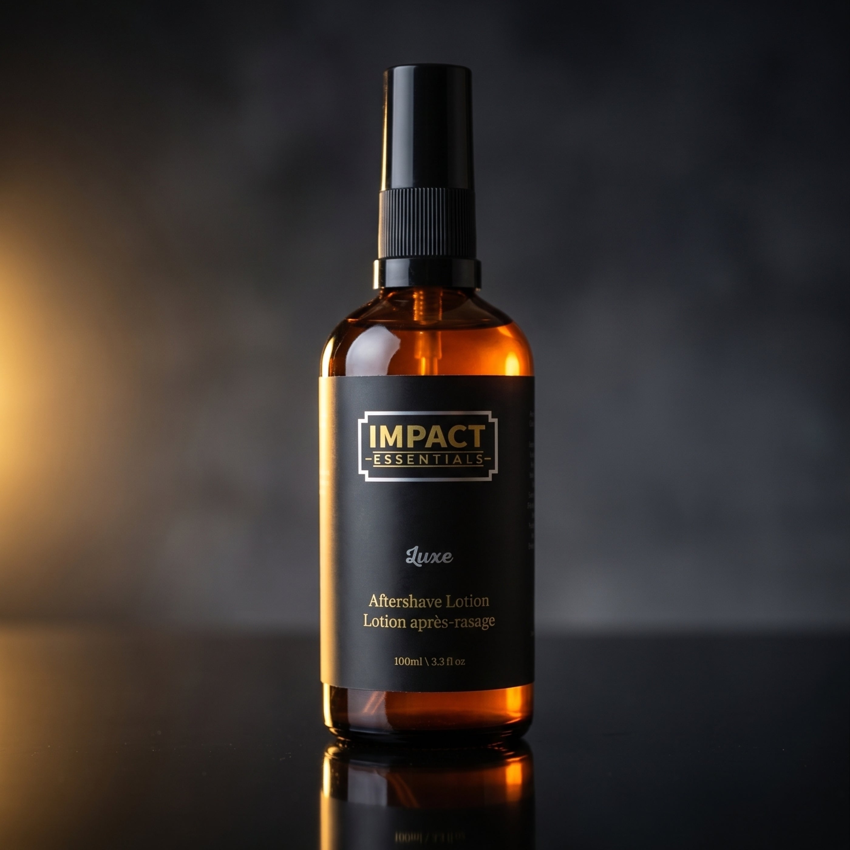 An amber glass spray bottle of Impact Essentials Luxe Aftershave Lotion with a black spray cap and black label, set against a dark, moody background with a warm light flare on the left.