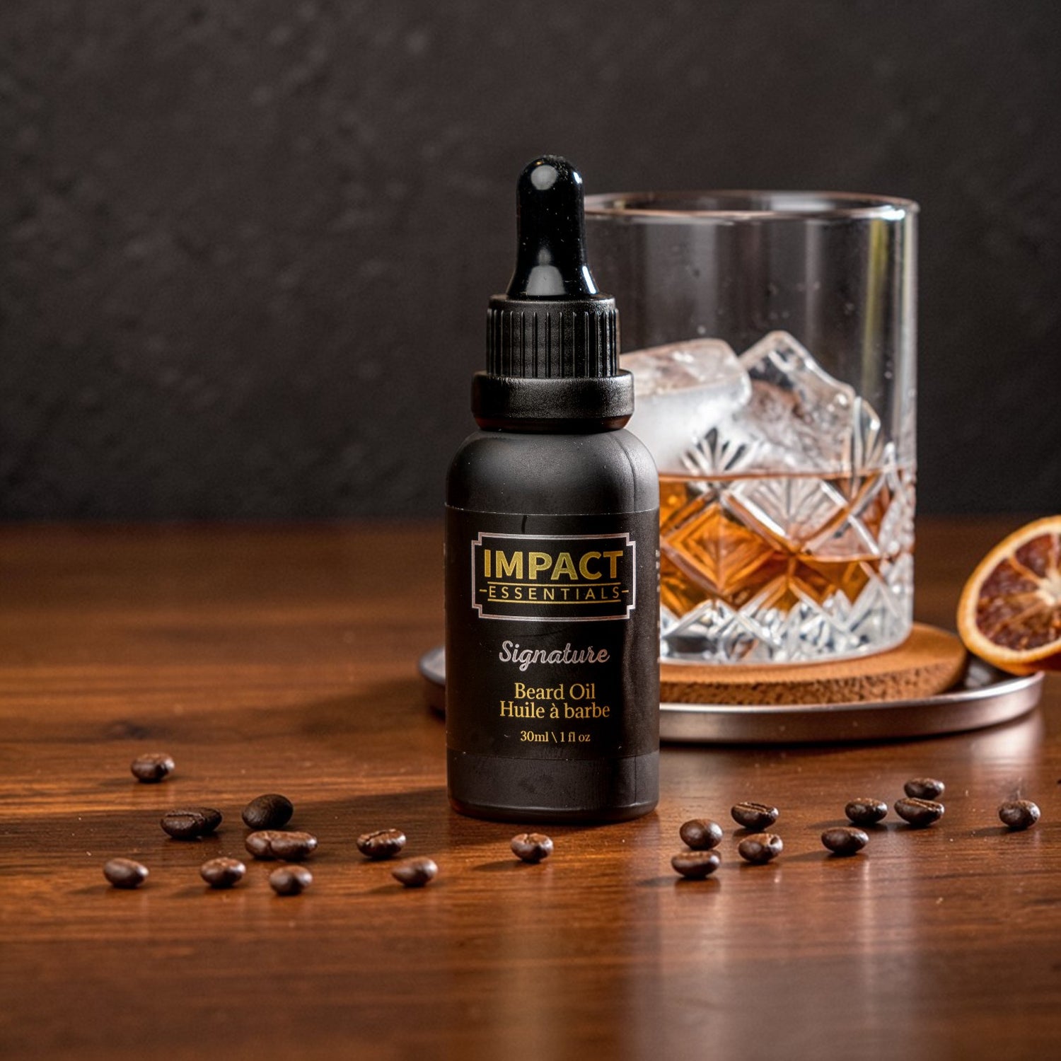 Bottle of Impact Essentials beard oil on a wooden surface with coffee beans and a glass of whiskey.