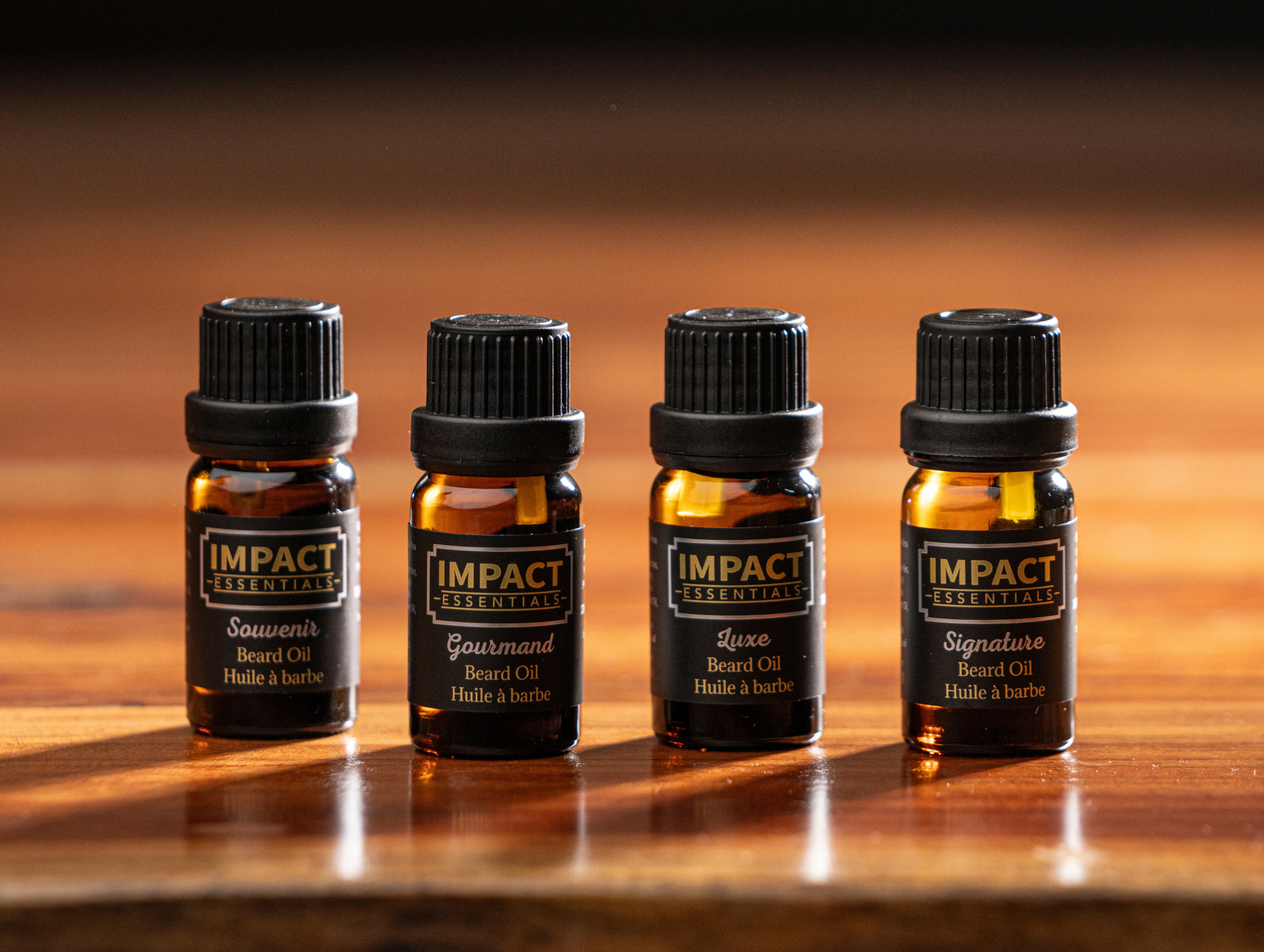 Four bottles of Impact Essentials beard oil on a wooden surface with a warm background.