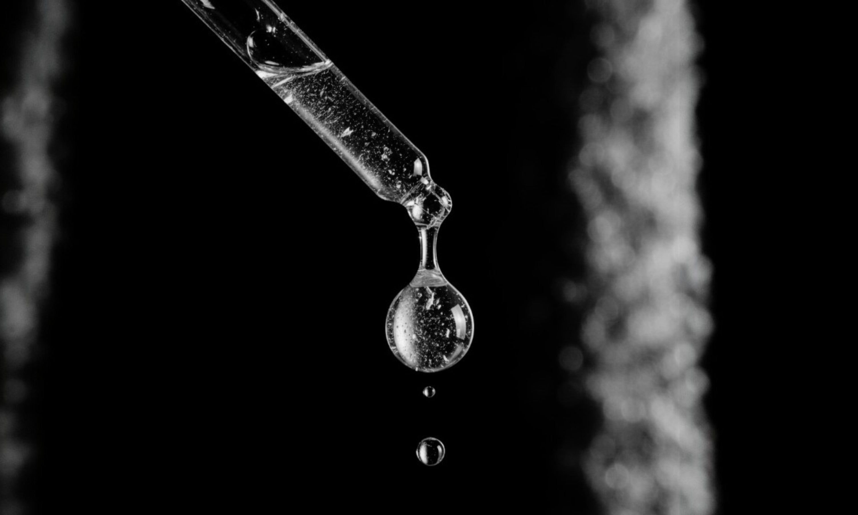 Close-up of a dropper with a drop of beard oil against a black background